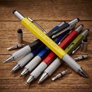 May include: A collection of multi-tool pens in various colors, including yellow, black, blue, red, and green, with silver accents. The yellow pen is inscribed with "CHARLOTTE MCCARTY". Each pen has a stylus tip and comes with small screwdriver bits.