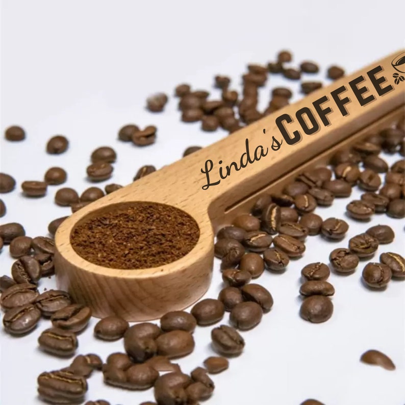 May include: A wooden coffee scoop with the text "Linda's Coffee" engraved on it. The scoop is filled with ground coffee and surrounded by coffee beans.