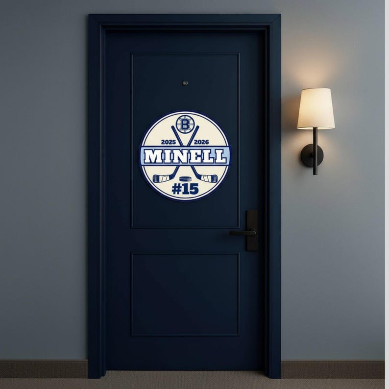 Peut inclure: Panneau de hockey circulaire avec le nom "MINELL" et le num&eacute;ro "15" en bleu et blanc. Le panneau comporte &eacute;galement des crosses de hockey et les ann&eacute;es 2025 et 2026. Le panneau est mont&eacute; sur une porte bleu fonc&eacute;.