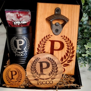May include: A gift set featuring a personalized wooden bottle opener, a personalized wooden coaster, and a personalized stainless steel tumbler. The bottle opener has a metal bottle opener attached to it. The coaster and tumbler both have the letter "P" and the word "PICCO" engraved on them.