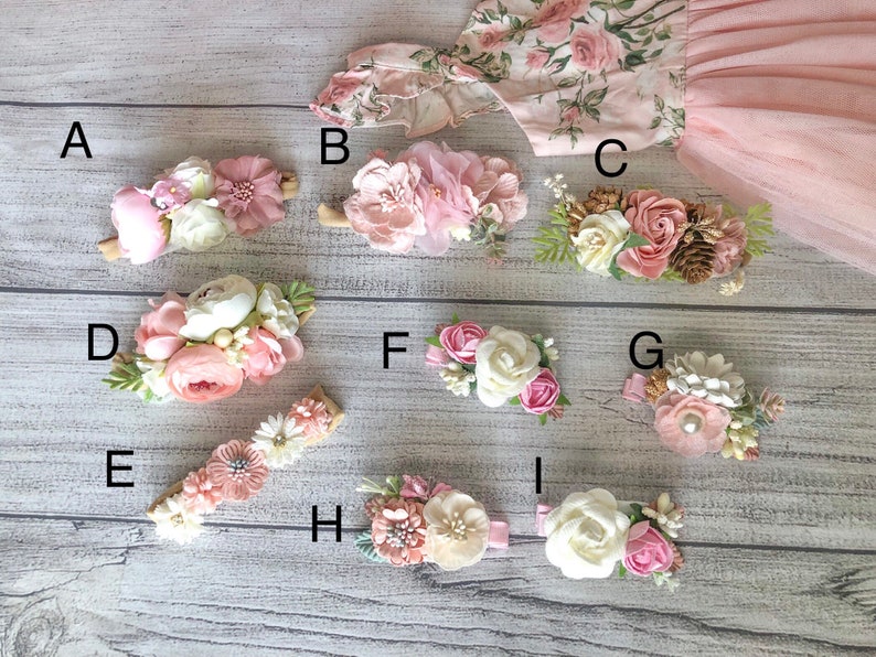 Op de afbeelding: Negen verschillende bloemenhaarclips met roze, witte en cr&egrave;mekleurige bloemen. De clips zijn gerangschikt op een houten oppervlak.