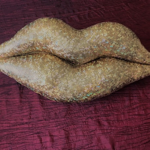 以下が含まれることがあります： 唇の形をした大きな金色クッション。クッションは鱗のような質感の表面をしています。