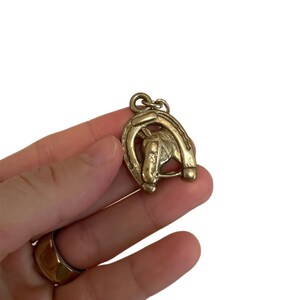 May include: A gold-colored metal pendant featuring a horseshoe and a horse head. The pendant is detailed with a textured finish and a loop for attaching to a chain or bracelet. The design is a classic equestrian theme.