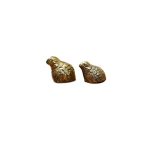 May include: Two small, detailed brass quail figurines. The birds are in a resting position, with textured feathers and a warm, metallic sheen. They are set against a plain white background, highlighting their intricate design.