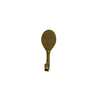 May include: A gold-colored metal wall hook shaped like a tennis racket. The racket head has a textured surface, and the handle curves down to form the hook. The hook is designed for hanging items and adds a decorative touch.
