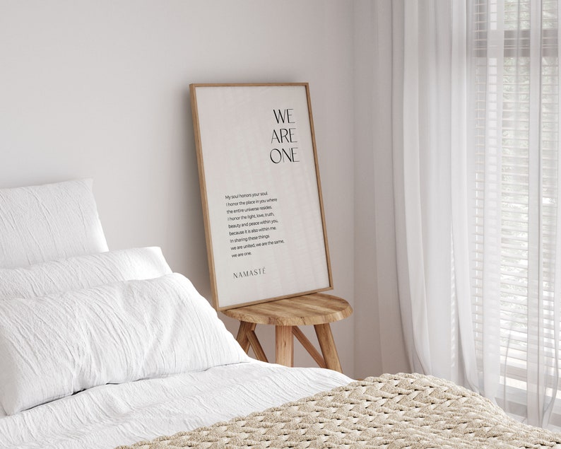 May include: A framed print with a white background and black text that reads "We Are One." The text is a poem about honoring the place in your soul where the entire universe resides. The print is hanging on a white wall above a wooden stool.