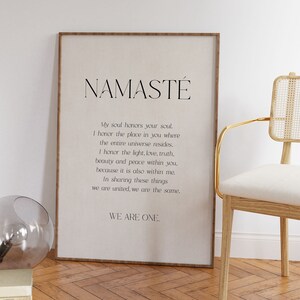 K&ouml;nnte beinhalten: Ein gerahmter Druck mit dem Wort "NAMAST&Eacute;" oben, gefolgt von einem Gedicht. Der Druck befindet sich in einem Holzrahmen und wird in der N&auml;he eines Stuhls mit goldenem Rahmen und einem dekorativen Glasobjekt ausgestellt.