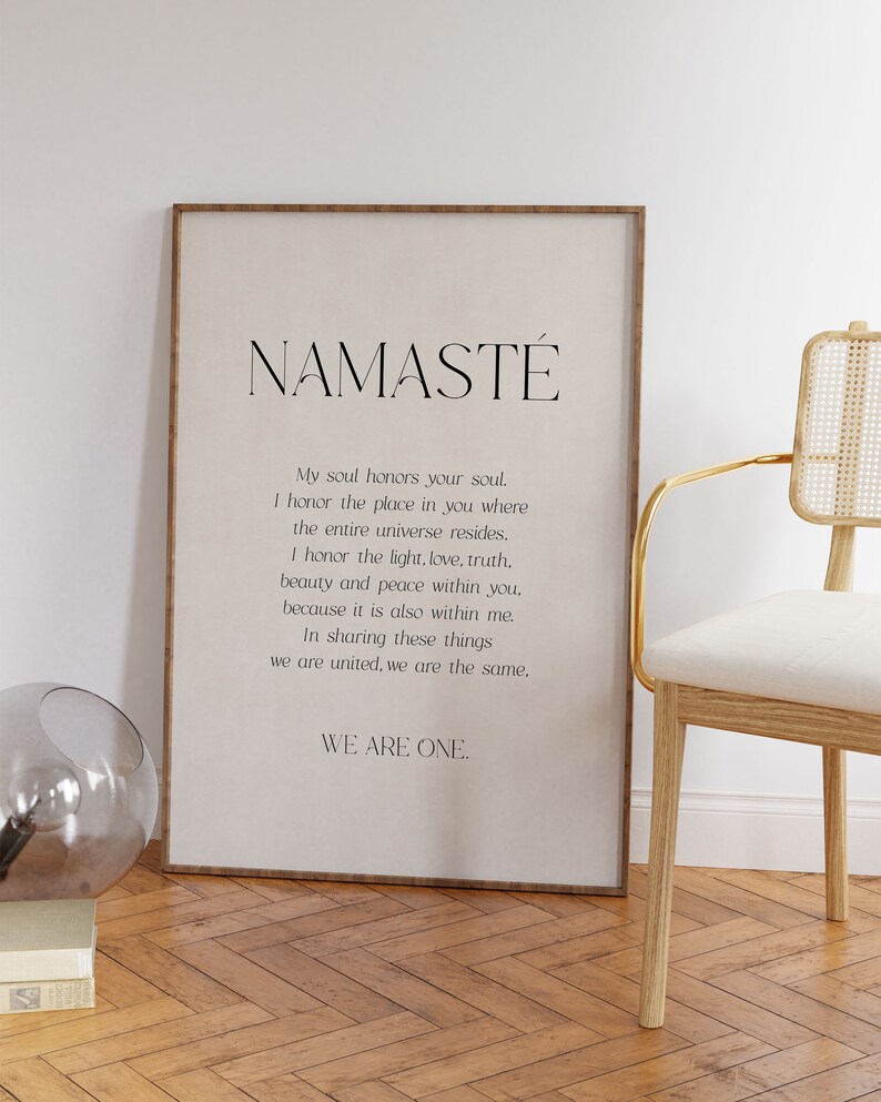 K&ouml;nnte beinhalten: Ein gerahmter Druck mit dem Wort "NAMAST&Eacute;" oben, gefolgt von einem Gedicht. Der Druck befindet sich in einem Holzrahmen und wird in der N&auml;he eines Stuhls mit goldenem Rahmen und einem dekorativen Glasobjekt ausgestellt.