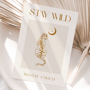 May include: A beige card with the text "STAY WILD" in gold lettering. A gold outline of a tiger looking up at a crescent moon with stars is in the center of the card. The text "MOON CHILD" is at the bottom of the card in gold lettering.