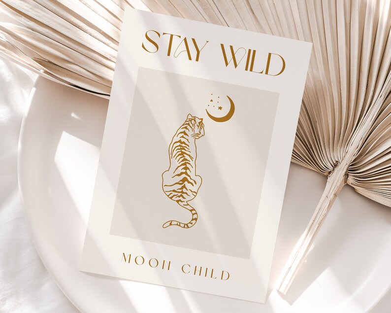May include: A beige card with the text "STAY WILD" in gold lettering. A gold outline of a tiger looking up at a crescent moon with stars is in the center of the card. The text "MOON CHILD" is at the bottom of the card in gold lettering.