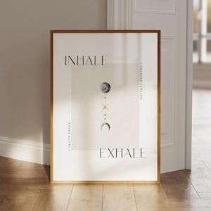 Könnte beinhalten: Ein gerahmter Druck mit minimalistischem Design, das die Wörter "INHALE" und "EXHALE" in schwarzem Text zeigt. Der Druck enthält auch einen stilisierten Mond und Sterne in Gold und Grau. Der Text "Ich lade Frieden ein" und "Ich löse Spannung" ist vertikal auf der linken und rechten Seite des Drucks geschrieben.