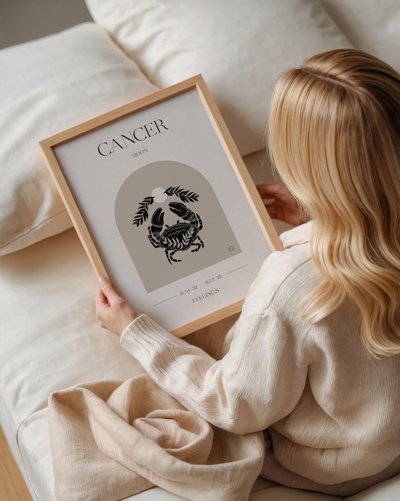 May include: A framed print with a minimalist design featuring the astrological sign Cancer. The print is in a light brown frame and has a beige background with a black crab illustration. The text "Cancer Moon" and "June 22 - July 22" is printed in black on the print. The text "Feelings" is printed in black at the bottom of the print.