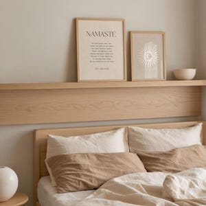 K&ouml;nnte beinhalten: Ein Schlafzimmer mit einem Bett mit beiger und wei&szlig;er Bettw&auml;sche, einschlie&szlig;lich Kissen und einer Bettdecke. &Uuml;ber dem Bett zeigt ein Holzregal zwei gerahmte Drucke mit Text und einem Sonnendesign sowie eine kleine wei&szlig;e Sch&uuml;ssel.