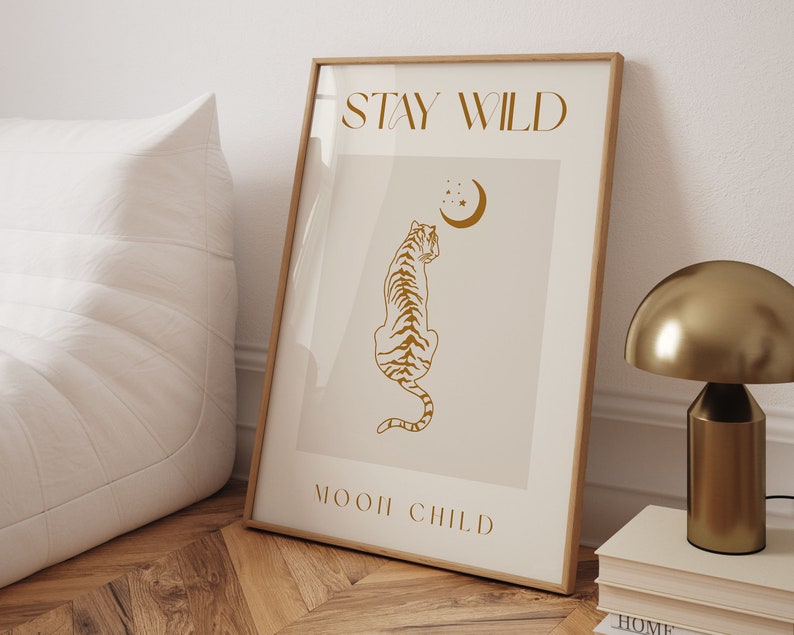 May include: A beige poster with a gold outline and the text "STAY WILD" and "MOON CHILD" in a gold script font. A gold silhouette of a tiger sitting and looking up at a crescent moon with stars is in the center of the poster.