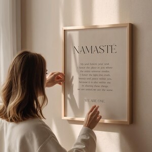 K&ouml;nnte beinhalten: Ein gerahmter Druck mit dem Wort "NAMASTE" oben, gefolgt von einem Gedicht. Der Rahmen ist aus hellfarbenem Holz. Der Druck wird von einer Person gehalten, die ein cremefarbenes Oberteil tr&auml;gt.