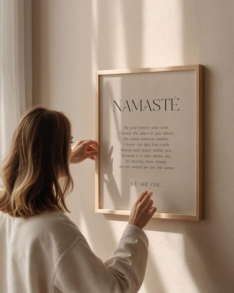 K&ouml;nnte beinhalten: Ein gerahmter Druck mit dem Wort "NAMASTE" oben, gefolgt von einem Gedicht. Der Rahmen ist aus hellfarbenem Holz. Der Druck wird von einer Person gehalten, die ein cremefarbenes Oberteil tr&auml;gt.