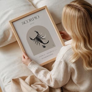 Puede incluir: Una impresi&oacute;n enmarcada con un dise&ntilde;o minimalista que presenta el signo del zod&iacute;aco Escorpio. La impresi&oacute;n est&aacute; en un marco de madera claro y tiene un fondo beige con una ilustraci&oacute;n de escorpi&oacute;n negro. El texto "Scorpio" y "Pluto" est&aacute;n impresos en negro en la parte superior de la impresi&oacute;n. Las fechas "October 23 - November 22" y la palabra "Transformation" est&aacute;n impresas en la parte inferior de la impresi&oacute;n.