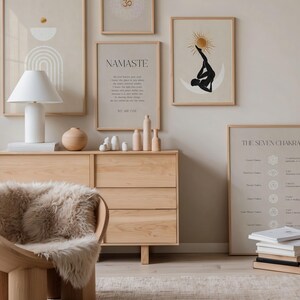 K&ouml;nnte beinhalten: Eine ruhige Innenszene mit gerahmten Kunstdrucken, einer Holzkommode und einem modernen Stuhl mit einem Kunstfell&uuml;berwurf. Die Kunstwerke umfassen abstrakte Designs und Yoga-Illustrationen. Eine wei&szlig;e Lampe und dekorative Holzobjekte erg&auml;nzen die beruhigende &Auml;sthetik.