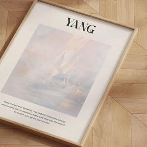 Op de afbeelding: Een ingelijste kunstdruk met het woord "YANG" in zwart bovenaan. Het kunstwerk heeft een zacht, abstract ontwerp in pastelkleuren. Tekst eronder beschrijft de energie van Yang. De lijst is lichtgekleurd hout.