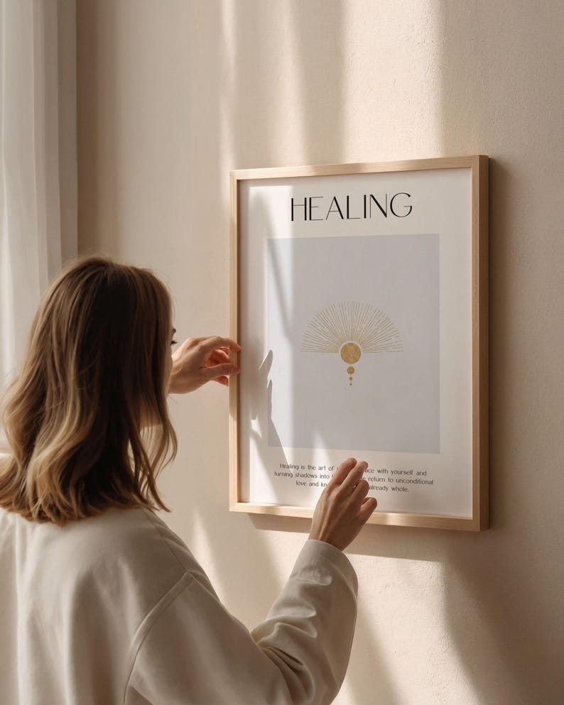 May include: A framed print with the word "HEALING" in black text at the top. The print features a stylized sunburst design in gold with a white background. The text below the design reads "Healing is the art of turning shadows into love and knowing peace with yourself and others. Return to unconditional love and be ready whole."