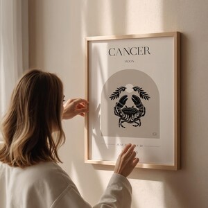 May include: A framed print with a minimalist design featuring the astrological sign Cancer, represented by a crab, with the text "Cancer Moon" above the image.