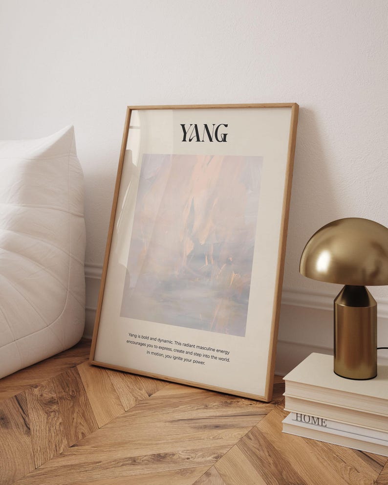 Op de afbeelding: Een ingelijste kunstafdruk met het woord "YANG" bovenaan. Het kunstwerk heeft een abstract ontwerp in tinten beige, blauw en oranje. De afdruk leunt tegen een witte muur en een houten vloer. Een gouden lamp en boeken zijn ook zichtbaar.