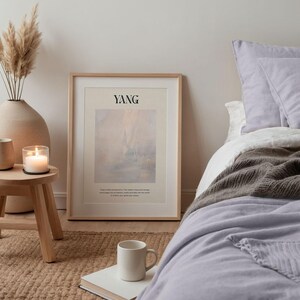 Op de afbeelding: Een slaapkamer met een ingelijste print met het woord "YANG" en een abstract landschap. De kamer omvat een bed met een lavendelkleurig dekbed, een witte mok op een boek en een kleine houten bijzettafel.
