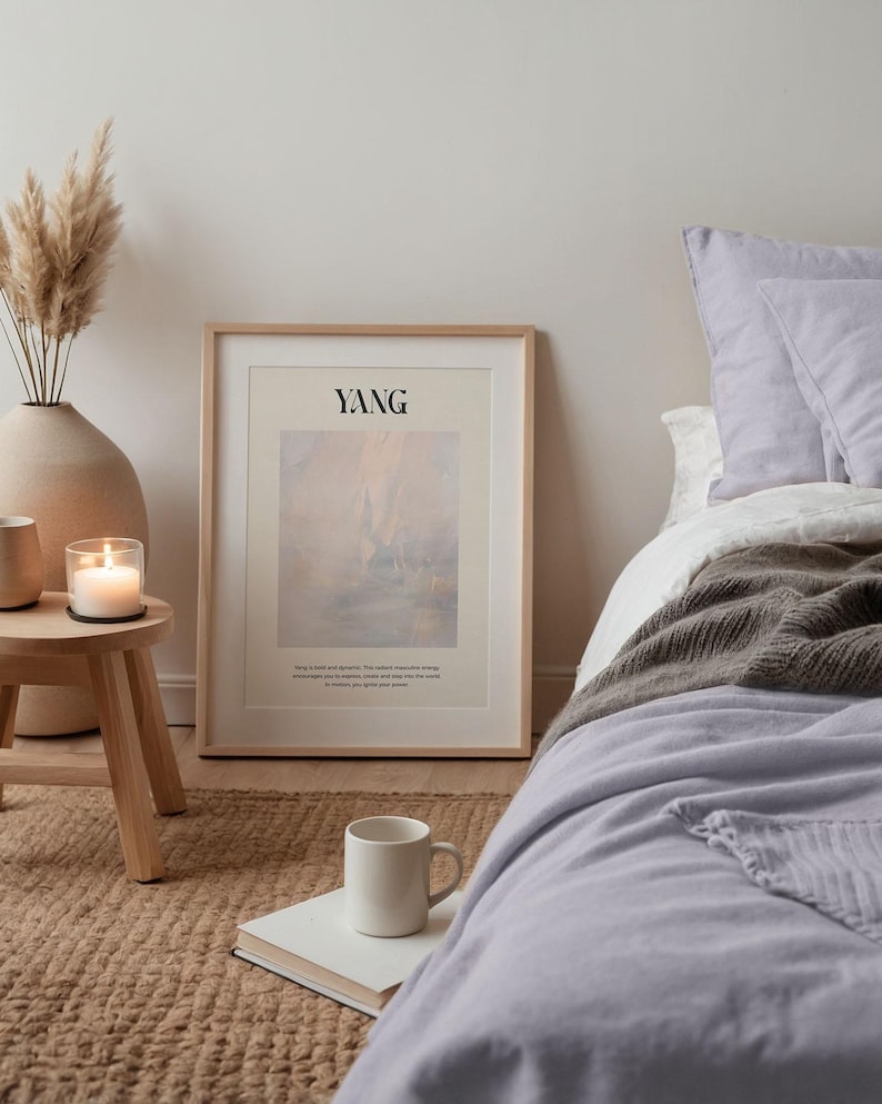 Op de afbeelding: Een slaapkamer met een ingelijste print met het woord "YANG" en een abstract landschap. De kamer omvat een bed met een lavendelkleurig dekbed, een witte mok op een boek en een kleine houten bijzettafel.
