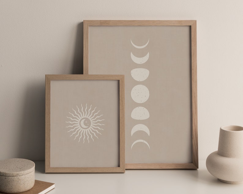 May include: Two framed prints with a beige background. The print on the left features a stylized sun with rays. The print on the right features a series of crescent moons in different phases.