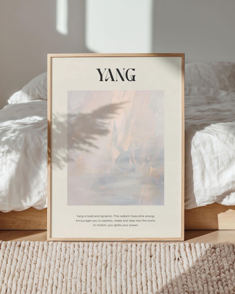 Op de afbeelding: Een ingelijste print met het woord "YANG" in zwart bovenaan. Het kunstwerk heeft een zacht, abstract ontwerp in tinten perzik, blauw en wit. De tekst hieronder beschrijft de energie van Yang. De lijst is licht van kleur.