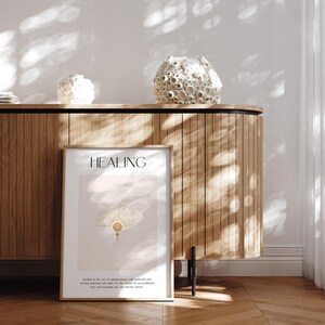 May include: A framed print with the word "HEALING" in black text at the top. The print features a gold sunburst design on a light pink background. The text below the design reads "Healing is the art of making peace with yourself and turning shadows into light. It's the return to unconditional love and knowing you are already whole."
