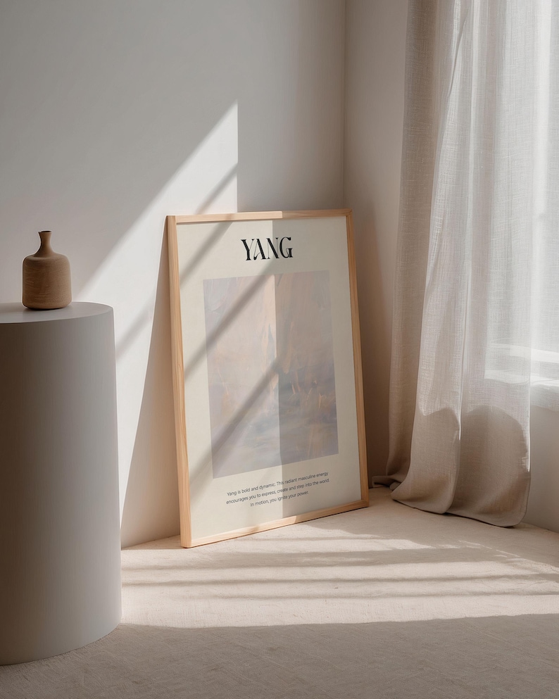 Op de afbeelding: Een ingelijste kunstprint met het woord "YANG" in zwarte letters. Het kunstwerk heeft een zacht, abstract ontwerp in gedempte tinten beige, roze en blauw. Een kleine, bruine keramische vaas staat op een witte sokkel. De print leunt tegen een muur.