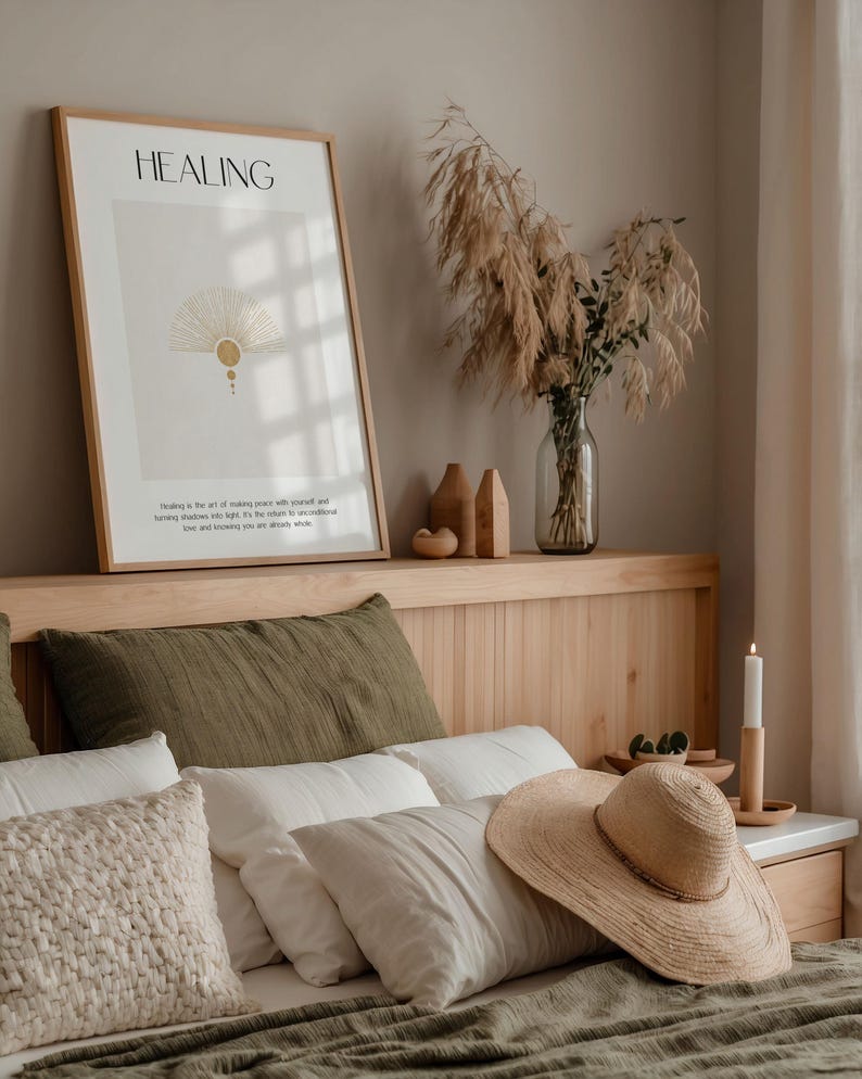 May include: A bedroom with a wooden headboard and a bed with green and white bedding. A framed print with the word "HEALING" and a quote about making peace with yourself is hanging on the wall above the headboard. A vase with dried pampas grass is on the headboard shelf. A straw hat is on the bed.