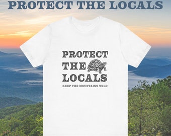 Puede incluir: Camiseta blanca con un estampado gráfico negro de una tortuga y el texto "Protect the Locals Keep the Mountains Wild".