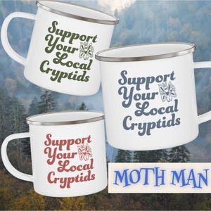 May include: White enamel mugs with silver rims and handles. Each mug features the phrase "Support Your Local Cryptids" in different colors: green, blue, and red. A butterfly graphic is included. The word "MOTH MAN" is also visible.