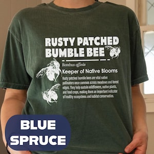 May include: Blue spruce t-shirt featuring the text "RUSTY PATCHED BUMBLE BEE" with bee illustrations and information about the species. The shirt also has the words "BLUE SPRUCE" at the bottom.