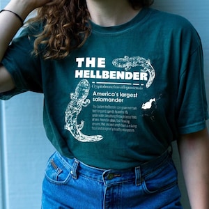 May include: Teal t-shirt with white text and illustrations. The shirt features the words "THE HELLBENDER" and "America's largest salamander" with a drawing of a salamander. Additional text describes the salamander's characteristics.