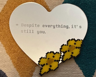May include: A heart-shaped mirror with the text "* Despite everything, it's still you."  Two yellow pixelated flowers are on the bottom right corner of the mirror.