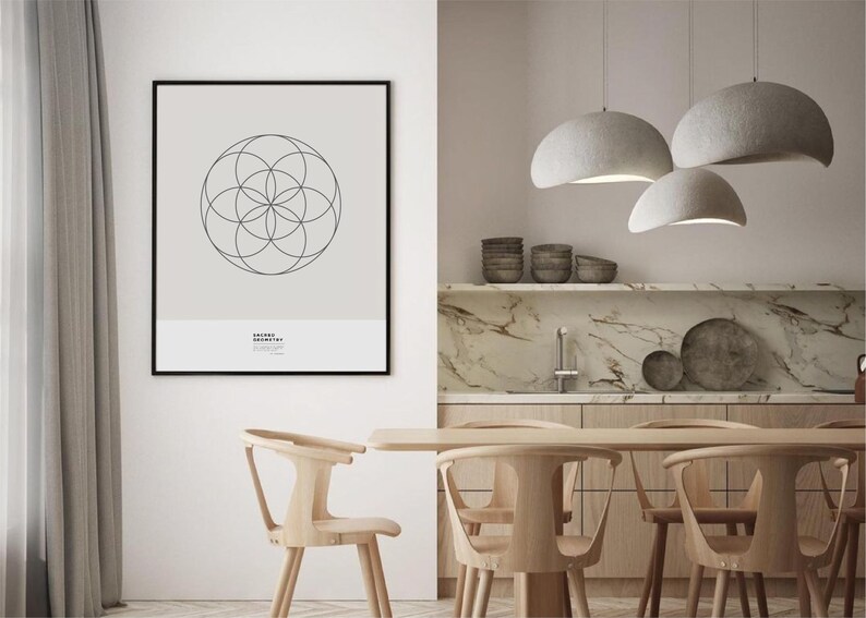 May include: A black framed print with a geometric design in a white room with a wooden dining table and chairs. Three gray pendant lights hang above the table.