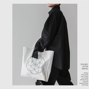 May include: A white tote bag with a black geometric design. The bag is being held by a person wearing a black shirt.