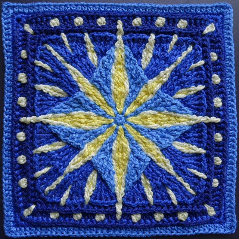 May include: A crocheted square with a blue and yellow starburst design. The starburst is made up of multiple layers of blue and yellow yarn, creating a 3D effect. The square is bordered with a white dotted trim.