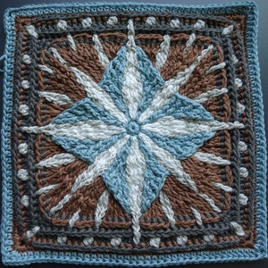 May include: A crocheted square with a starburst design in shades of brown, blue, and white. The center of the starburst is a white circle surrounded by blue and white stripes. The outer edges of the square are a dark gray border with white dots.