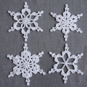 Peut inclure: Quatre flocons de neige en crochet blanc sur un fond de tissu gris.