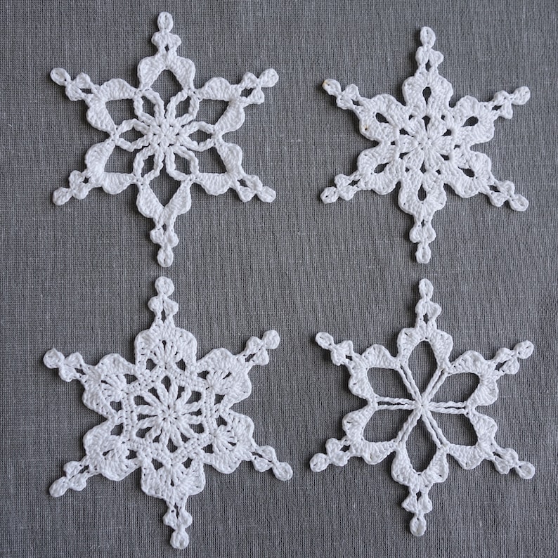 Peut inclure: Quatre flocons de neige en crochet blanc sur un fond de tissu gris.