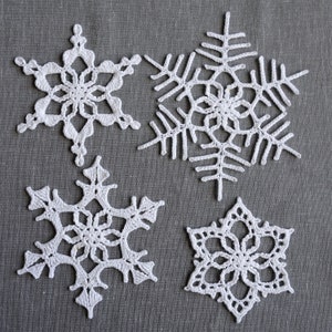Peut inclure: Quatre flocons de neige en crochet blanc sur un fond de tissu gris. Les flocons de neige sont de tailles et de motifs diff&eacute;rents.