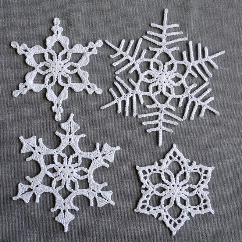 Peut inclure: Quatre flocons de neige en crochet blanc sur un fond de tissu gris. Les flocons de neige sont de tailles et de motifs diff&eacute;rents.