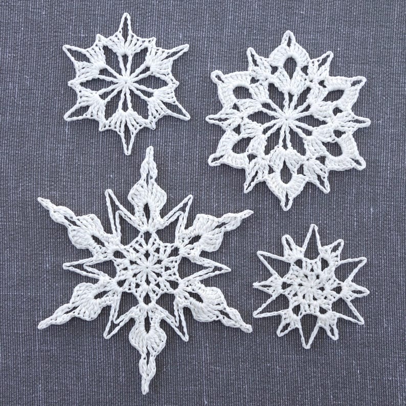 May include: Four white crocheted snowflakes of varying sizes on a gray textured background.