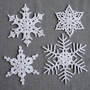 Peut inclure: Quatre flocons de neige en crochet blanc sur un fond de tissu gris. Les flocons de neige sont de tailles et de motifs diff&eacute;rents.