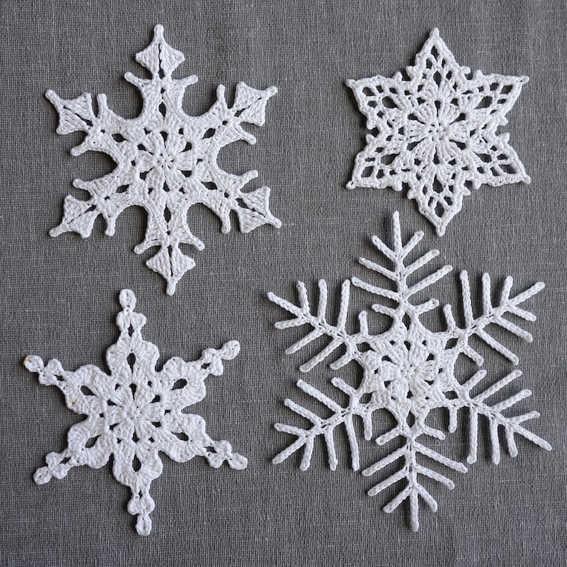 Peut inclure: Quatre flocons de neige en crochet blanc sur un fond de tissu gris. Les flocons de neige sont de tailles et de motifs diff&eacute;rents.