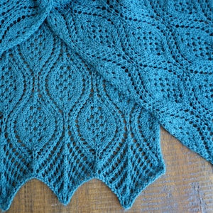 May include: Teal blue crocheted shawl with a lacy pattern. The shawl is folded in half and the edges are scalloped.
